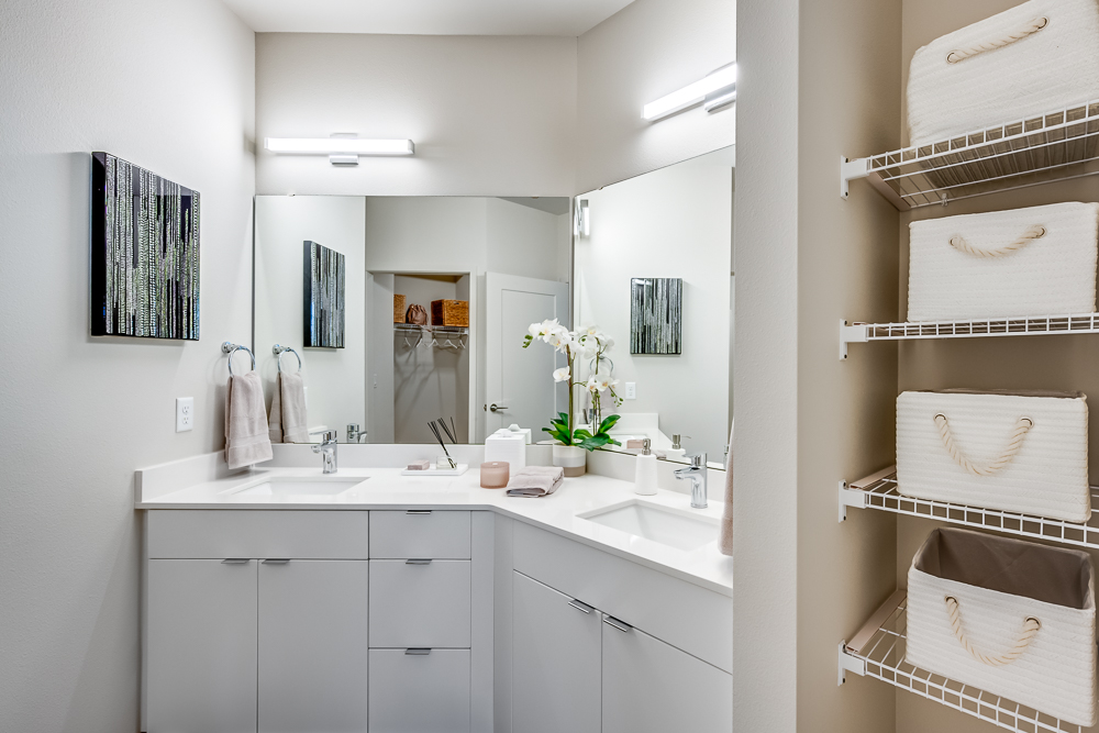 Bathroom with two sinks, large mirrors, and plenty of storage space in an apartment at The Woods at Alderwood in Lynnwood, WA.