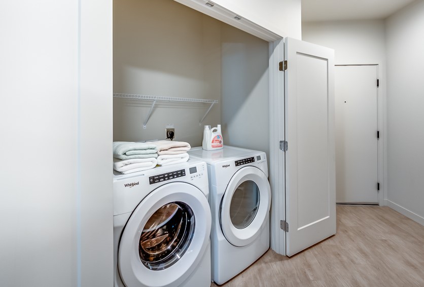 In-unit laundry closet with washer, dryer, and shelf at The Woods at Alderwood in Lynnwood, WA.